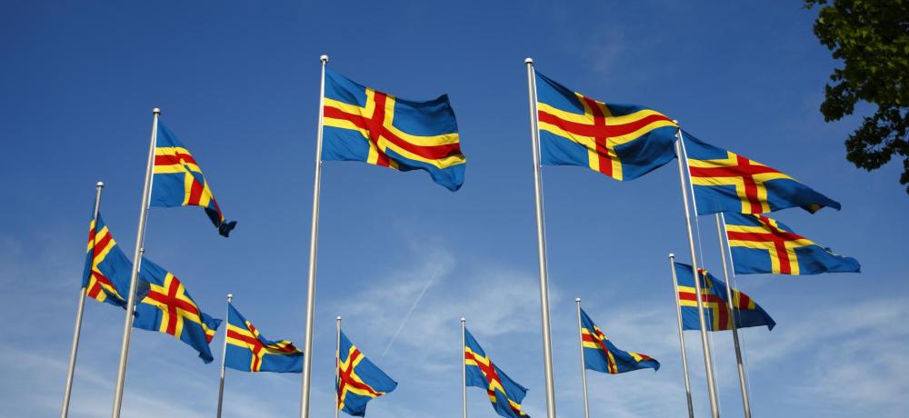Åländska flaggor fladdar i en ring mot en blå himmel.