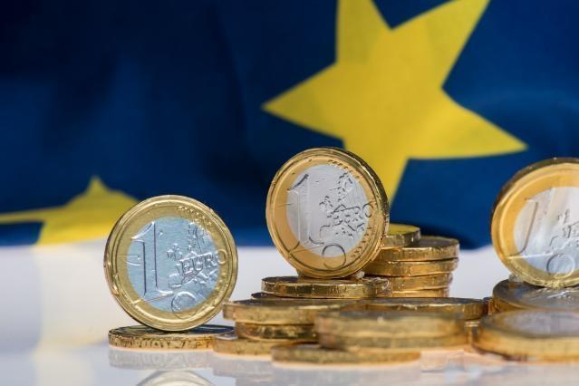 Euromynt, i bakgrunden ser man delar av en EU-flagga.