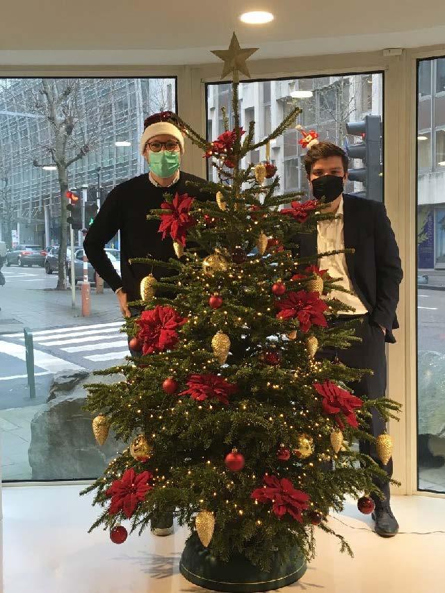 Anton och John står bakom en fint klädd julgran, de bär båda ansiktsmask.