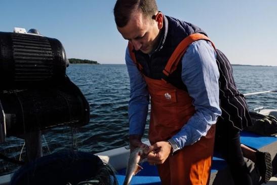 Kommissionären Virginijus Sinkevičius står i en båt med en fisk i handen.