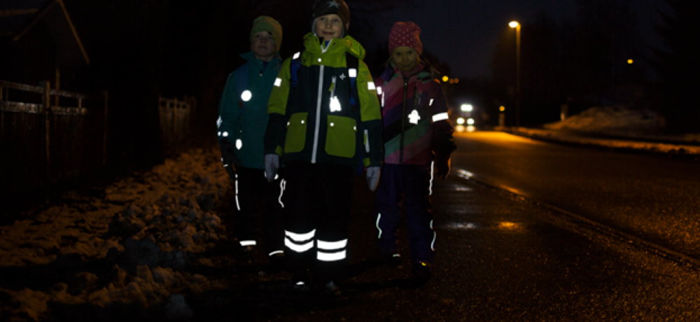 Tre barn använder reflexer i mörkret på en väg