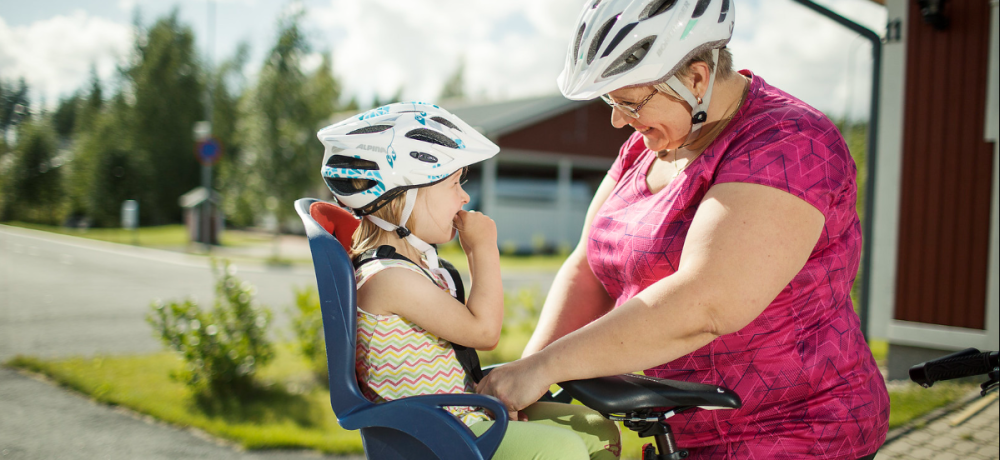 mormor spänner fast barnbarn i cykelstol, båda har cykelhjälm