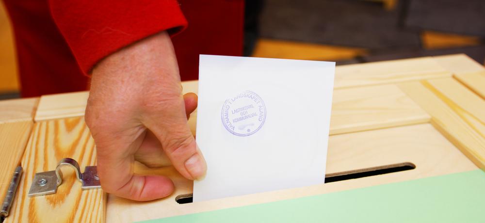 En hand som lämnar röstsedel i valurna