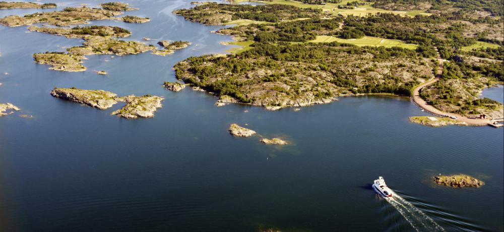 Flygbild över Ålands skärgård med en båt kryssandes in mot hamn